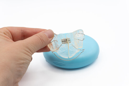 hand showing a clear dental retainer or palate expander for orthodontic treatment, next to its protective blue storage case