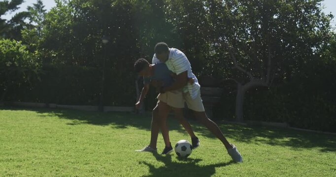 African American dad and child playing on lawn, dad coming right, tussling over soccer ball