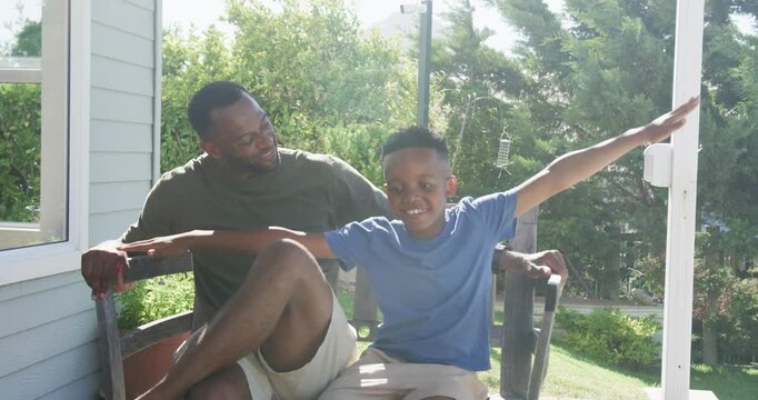 African American father and son playing on porch bench, boy pretending flight, father keeping safe