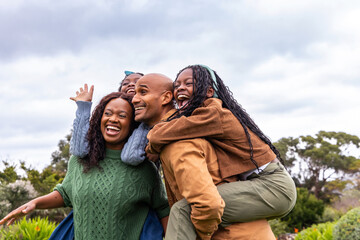 Naklejka premium African American family posing in park, man in tan jacket holding laughing child with headband