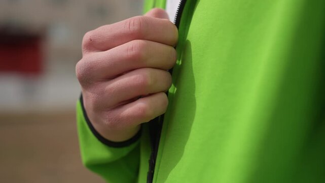 jacket zipper contact, detailed image showing hand fastening zipper on green jacket during urban commute, closeup shot capturing hand adjusting zipper on green outerwear before city journey