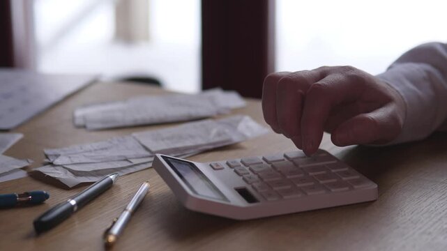 Closeup Hands Tallying Receipts With Calculator, Fingers Pressing Keys Over Scattered Invoices And Pens, Small Business Owner Reconciling Expenses, Soft Backlight And Warm Wood Desk Mood