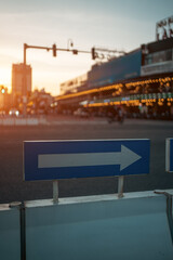 Directional arrow road sign at urban intersection during warm sunset at city atmosphere, Traffic guidance pointer on street with golden evening light and blurred city background
