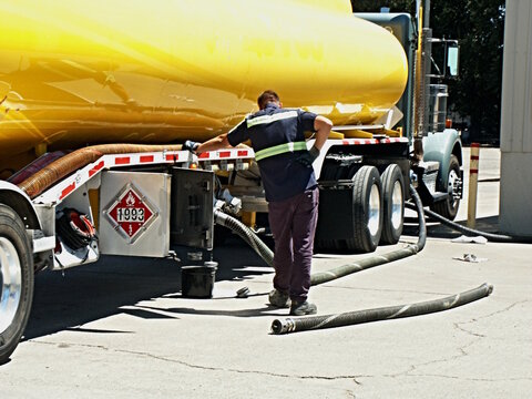 Driver in yellow vest watches process of off loading diesel fuel at customer facility, with hazmat placard.