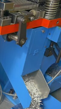 Industrial automatic sheet stamping machine actively forming metal sheets. A stream of small, gleaming metal offcuts cascades into a collection chute.