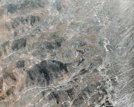 Aerial view of winding, pale trails etched across the rough, grey-brown landscape, creating a stark contrast between the natural terrain and the paths, Iceland.
