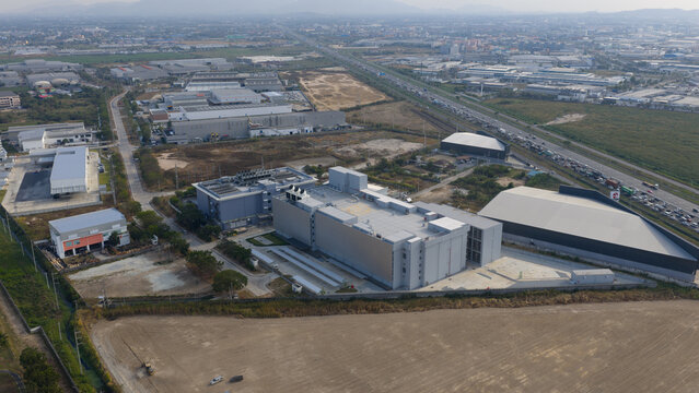Aerial view of the sprawling industrial landscape, revealing a modern data center amidst the infrastructure, casting shadows on the muted earth, Chang Wat Chon Buri, Thailand.