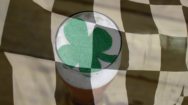 Checkered cloth rippling in breeze drifting over pint glass revealing tilting shamrock showing beer
