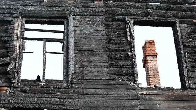 Burnt house facade showing charred wood wall and window frames after fire