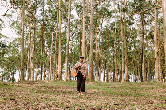 Person standing barefoot with guitar in forest