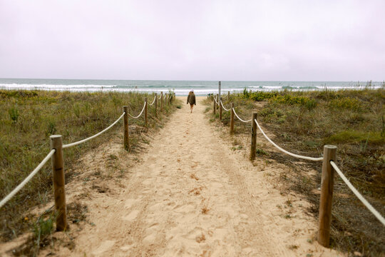 Person walking alone towards the sea along a sandy path