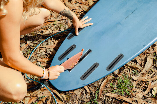 Woman attaching fin to blue surfboard outdoors