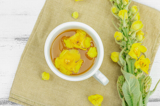 Cup of herbal tea with mullein flowers and leaves on neutral wooden background. Natural light