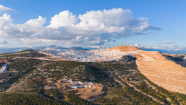 The majestic appearance of the marble quarry on a cloudy day. The contrasting overall view of the reforestation at the foot of the mountains and the mining area.