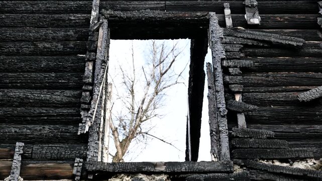 Charred wooden logs forming wall of a burnt house, with an empty window frame