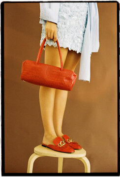Woman standing on stool holding red handbag