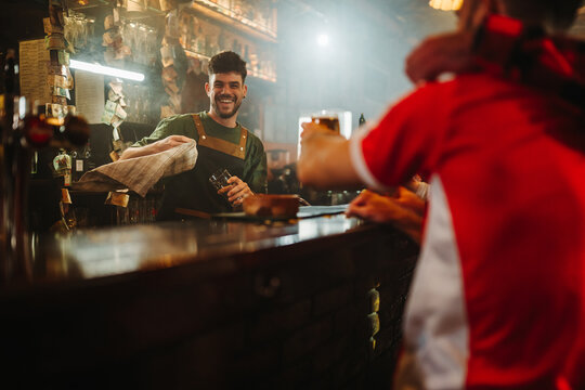 Friendly bartender serving customer at busy pub