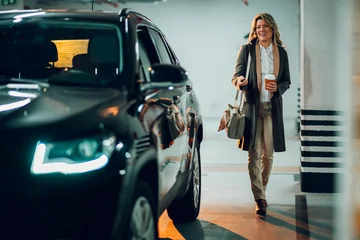 Fototapete Rund Restaurant Professional woman arriving at or leaving her car in a modern underground parking garage, holding coffee and a car key  © Zamrznuti tonovi