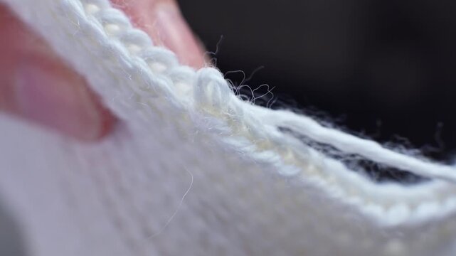 Close-up of hand stitching white yarn through knitted fabric, showcasing the detailed process of creating a seamless edge in textile crafting