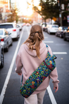 Woman walking on city street with yoga mat carrier
