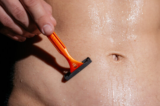 A young man shaves his belly skin with a shaving machine. A guy with a prominent torso is getting ready for a date or surgery. Concept: skin care, skin damage or disease. the athlete prepares for the 