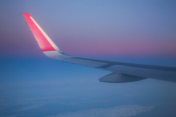 Obraz premium The wing of a flying airplane in the morning against the sky