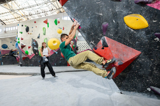 Man bouldering at indoor climbing gym, woman watching