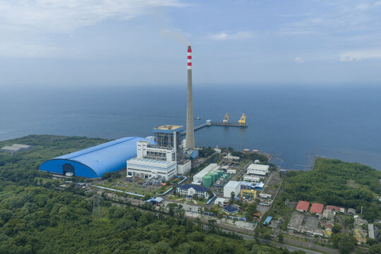 Aerial view of a power plant with a tall chimney stands in stark contrast to the blue sea, Jakarta, East Java, Indonesia.