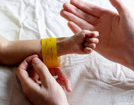 Father holds little hand of newborn with bracelet on his arm