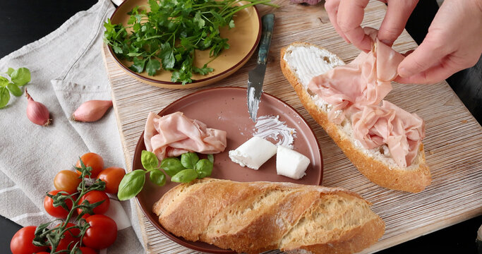Anonymous person prepares sandwich with cheese, basil, and mortadella in kitchen. Italian cuisine, high-quality farm-to-table ingredients.
