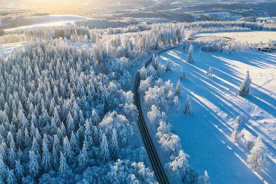 Aerial view of a winding road cutting through a snow-laden forest, the crisp white contrasting against the dark asphalt, Winterberg, North Rhine-Westphalia, Germany.