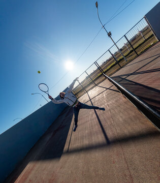 Tennis Player Serves Under a Clear Sky in Afternoon Light