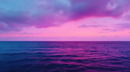 Obraz premium A tranquil ocean at sunset with a vibrant purple and pink sky reflecting on calm waters.