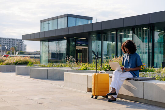 Woman Traveler Sitting Outdoors with Luggage and Laptop