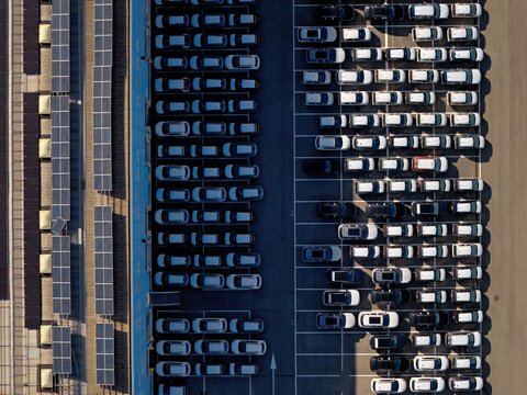 Aerial view of neatly arranged rows of parked cars casting long shadows, juxtaposed with solar panels, creating a geometric dance of light and dark, Civitavecchia, Lazio, Italy.