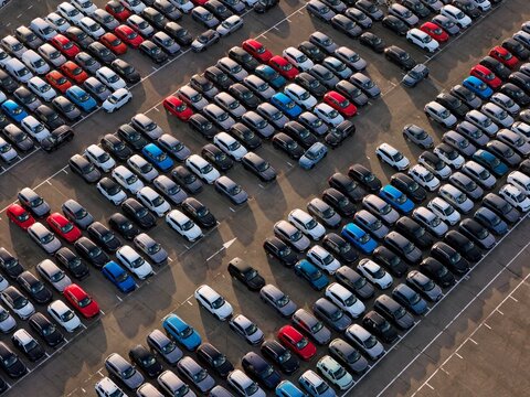 Aerial view of a sea of colorful cars parked in neat rows, creating a vibrant tapestry of hues against the stark asphalt, Civitavecchia, Lazio, Italy.