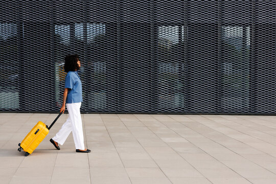 Woman pulling suitcase past modern building