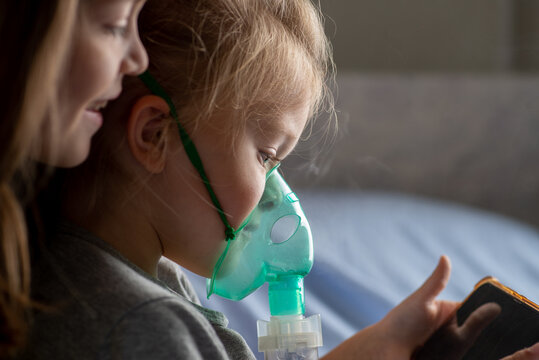 Older child helps the younger one do inhalation with a mask.
