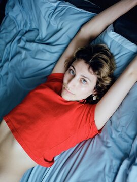 Portrait of a caucasian woman in a red top on a bed.
