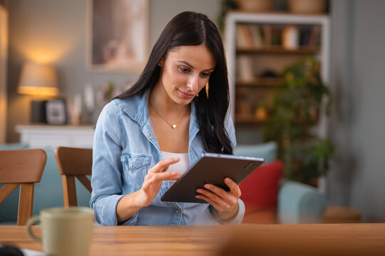 Woman browsing digital tablet at home kitchen table