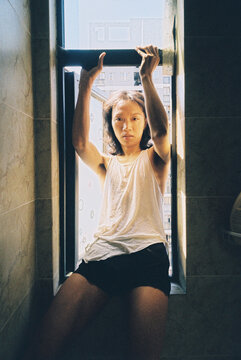 Man sitting on the edge of a window facing inwards on a sunny day