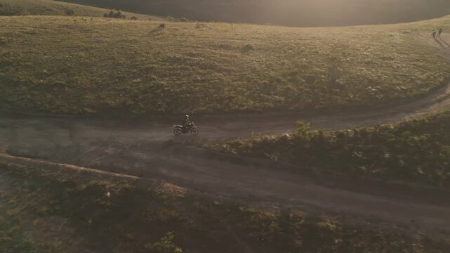 Vista a&eacute;rea de uma mulher pilotando uma motocicleta em uma estrada de terra no alto da montanha