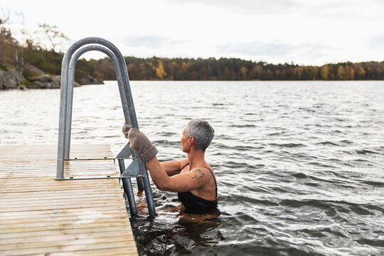 Active mature Woman Cold Plunging in Autumn Lake