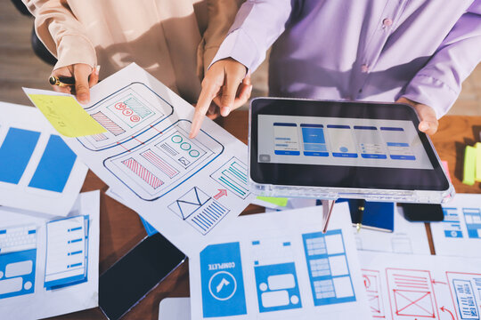 Close up ux developer and ui designer brainstorming about mobile app interface wireframe design on table with customer breif and color code at modern office.Creative digital development agency.
