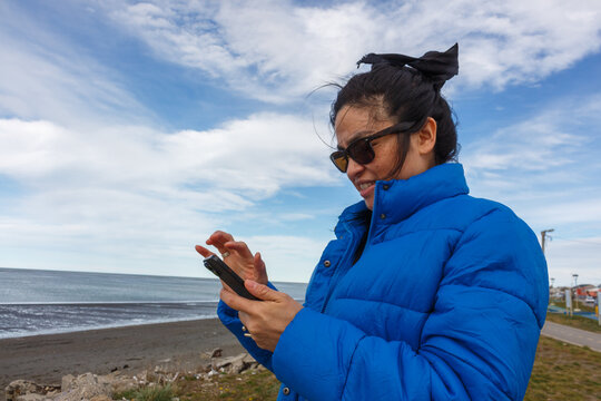 Woman Using Smartphone by the Beach on a Cloudy Day