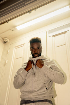 Man Adjusts Hoodie in Front of Closed Doors at Night