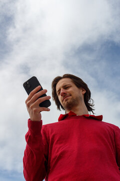 Man Holding Smartphone Against a Cloudy Sky During Daytime