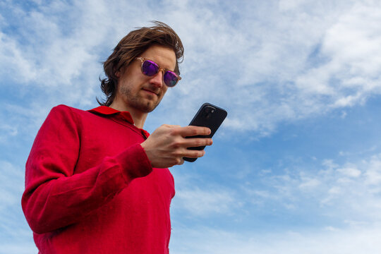 Man in Red Sweater Using Smartphone Against a Cloudy Sky