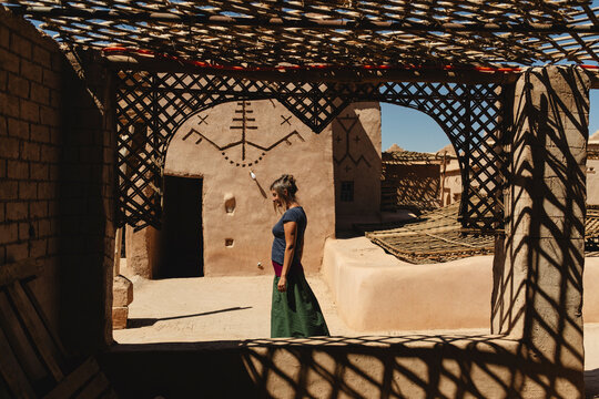 Woman Walking on Kasbah Rooftop with Berber Symbols on Walls