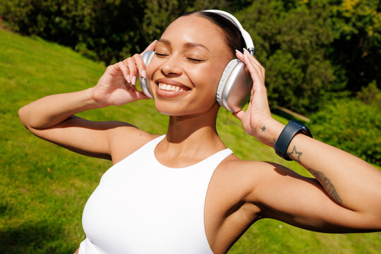 Joyful Woman in Headphones Standing on Sunny Grass